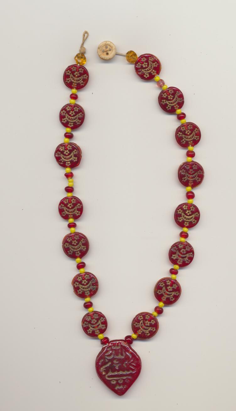 A very asymmetric old necklace for a child of flat red Islamic ''Hajj'' Czech molded glass beads and amulet pendant, from the Middle East, length necklace 13'' 34cm., pendant 1'' 3cm. A button and loop closure is used as fastener.